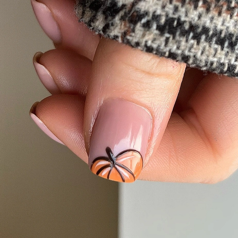 Short pink nails with one tiny orange pumpkin accent