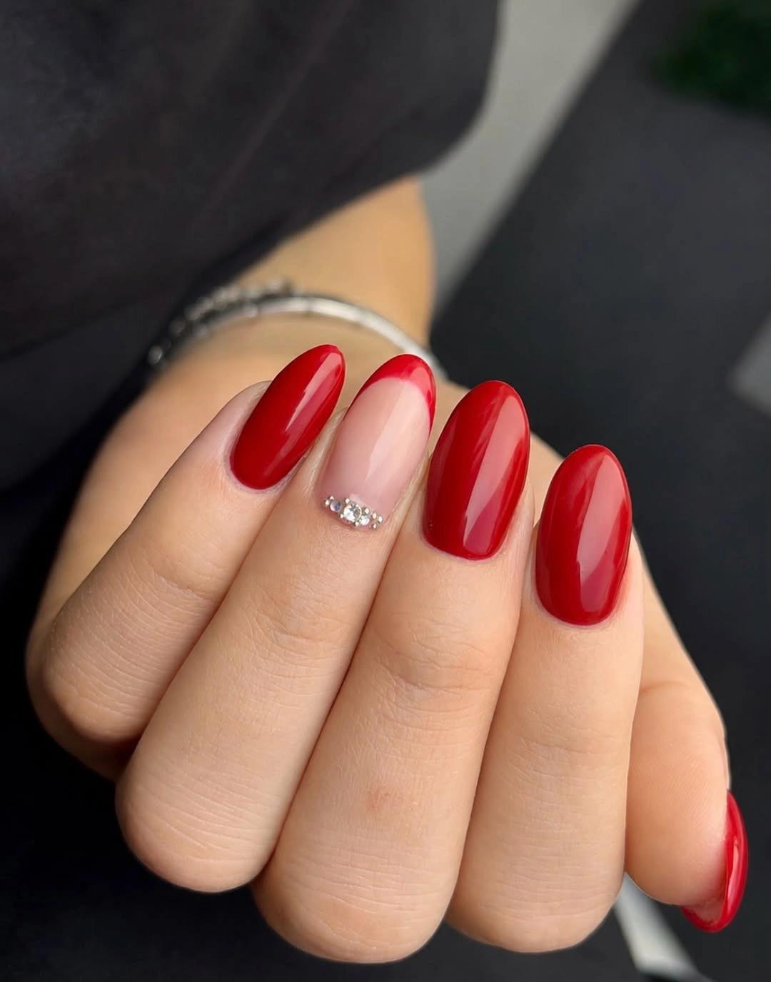 Glossy red almond nails with nude crystal accent