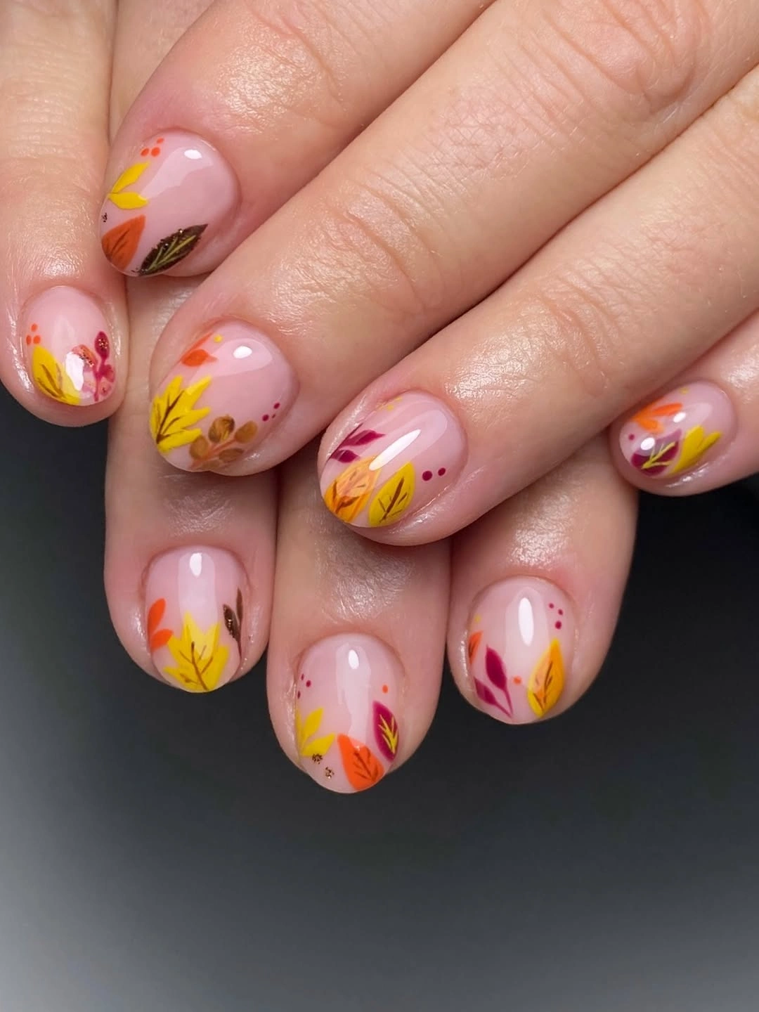 Blush short almond nails with tiny yellow and coral leaf motifs