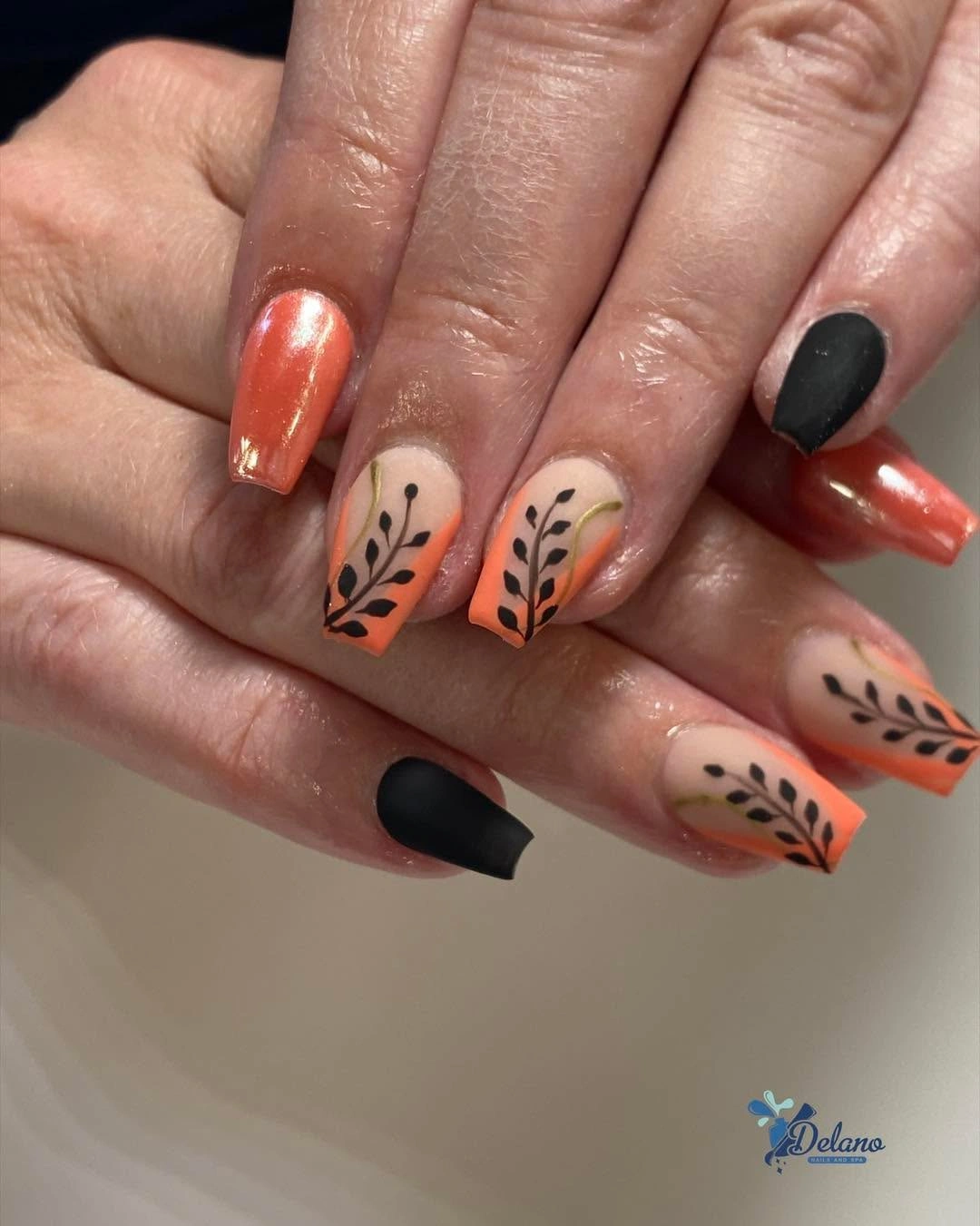 Short coral orange nails with black botanical branch accents