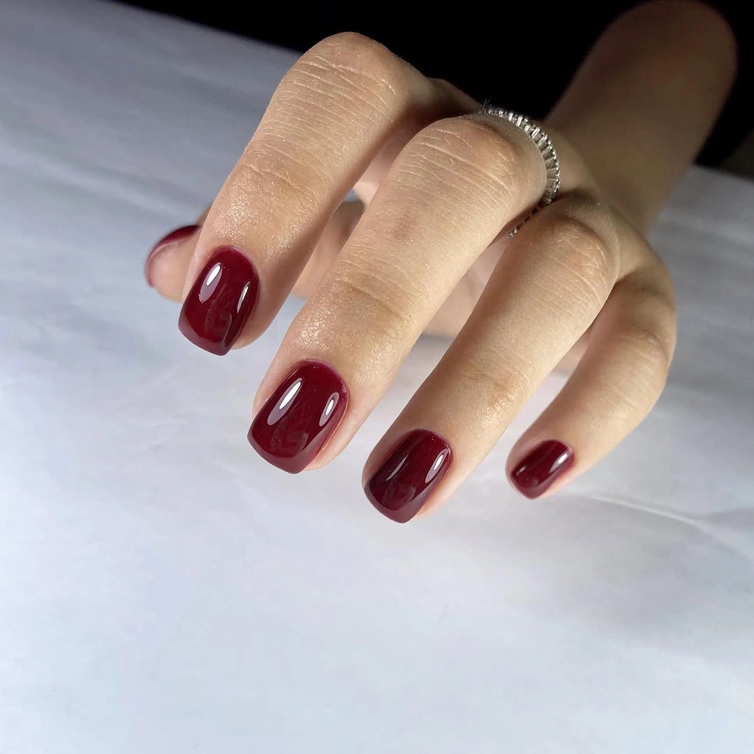 Short rounded nails in a uniform glossy deep wine burgundy shade