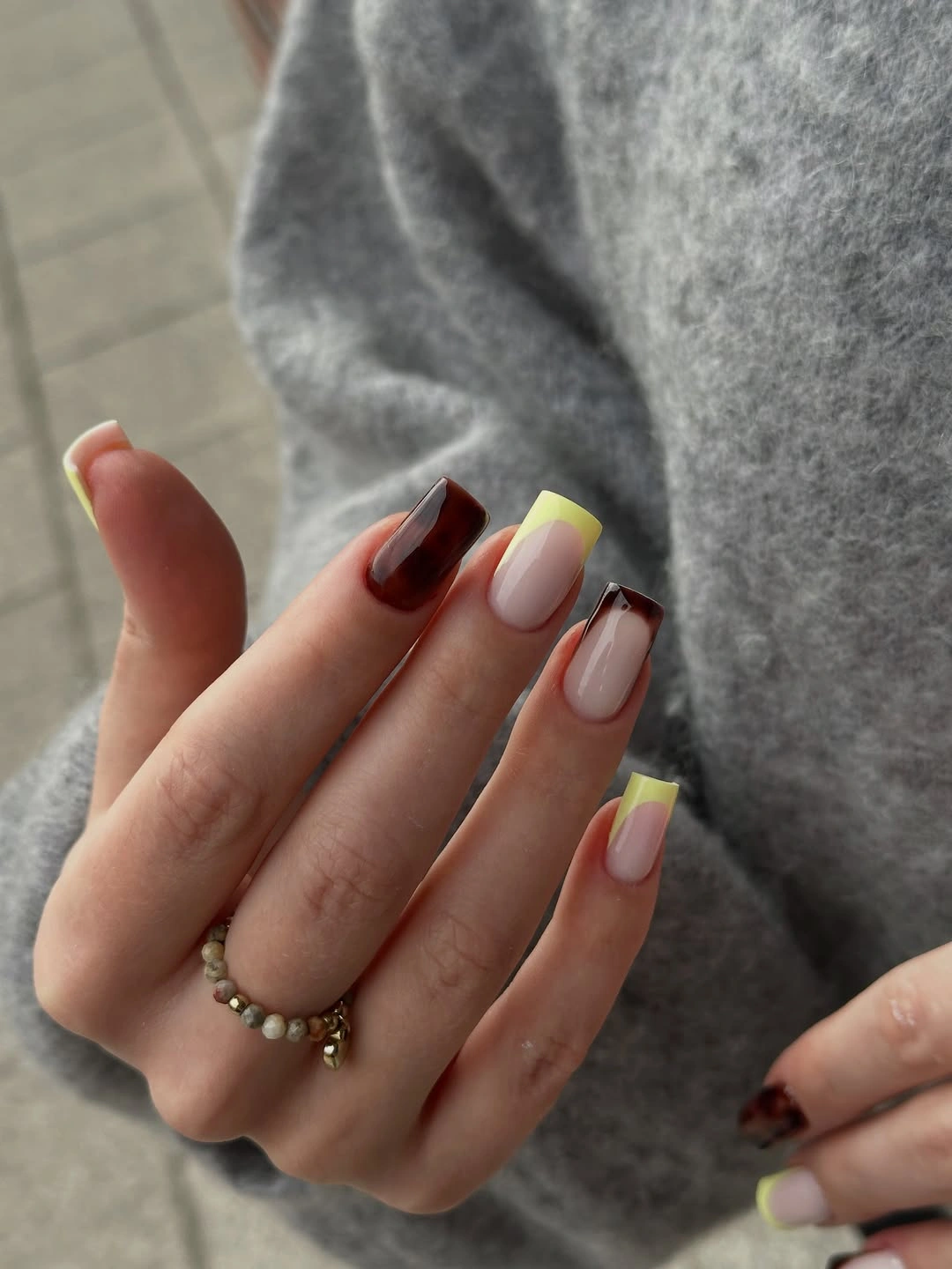 Sheer nude square nails with dark corner marks and pale yellow accents