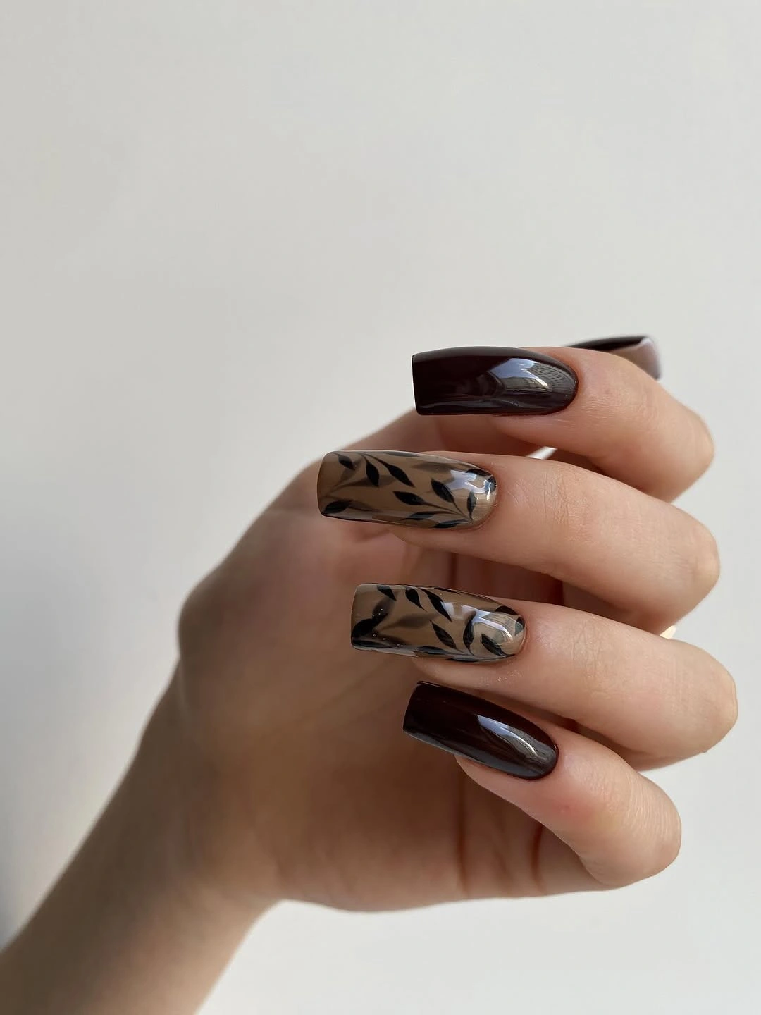 Rounded burgundy nails with taupe and black striped accents