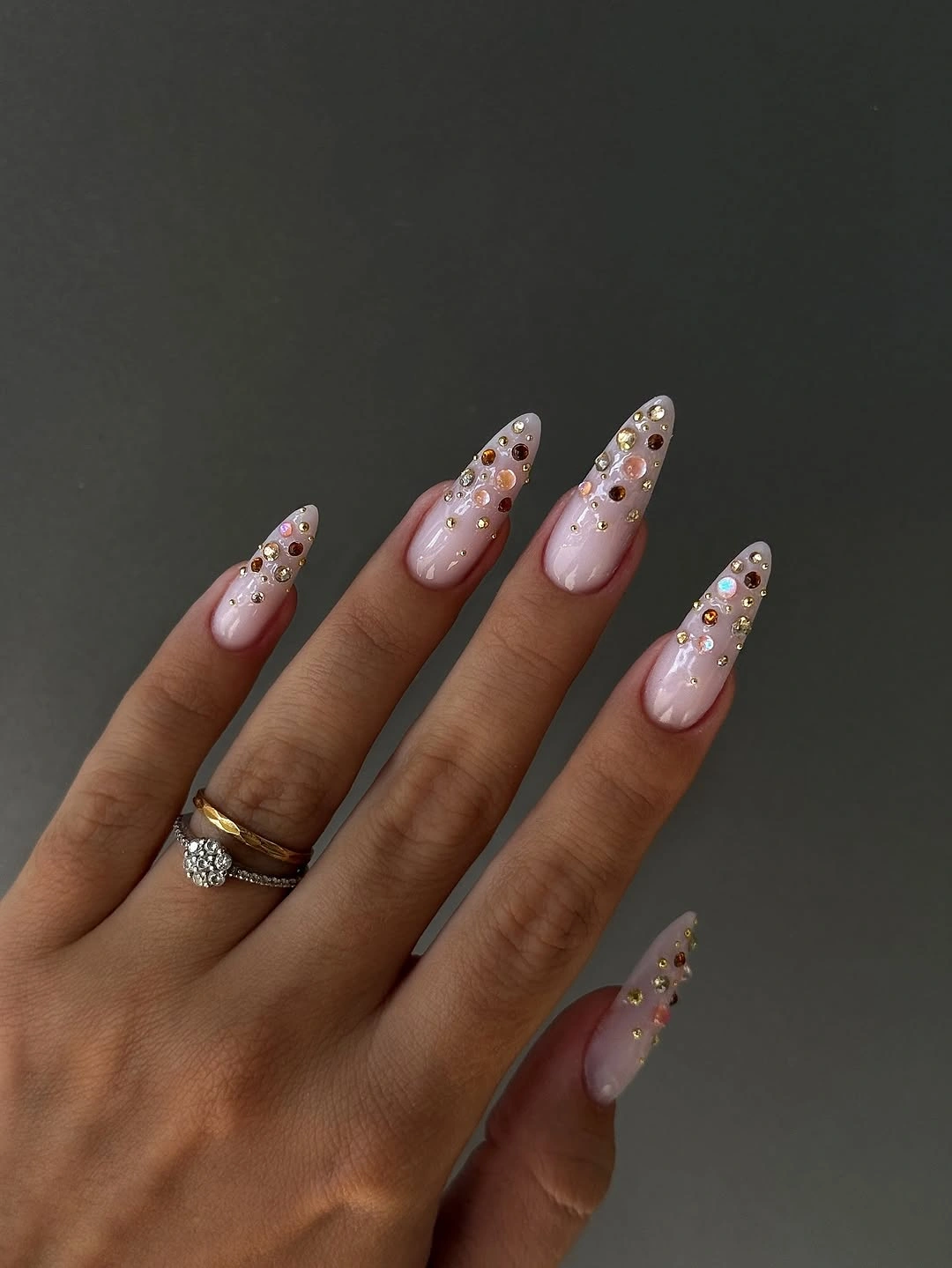 Sheer pink pointed nails with warm crystal like clusters