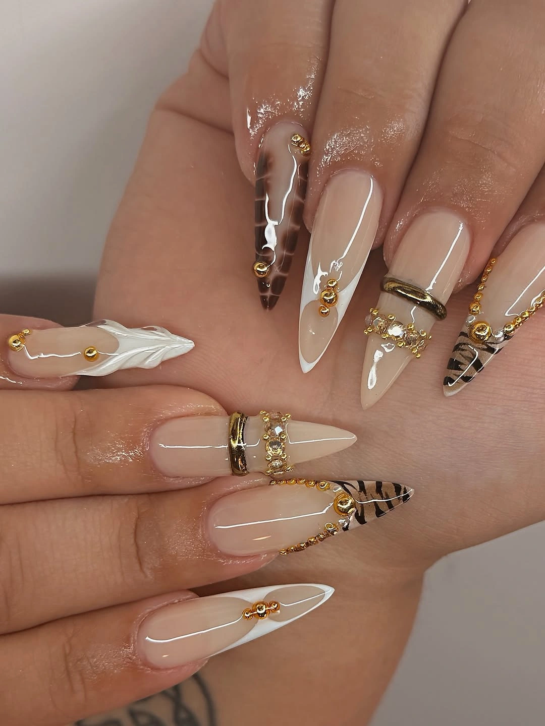 Long nude stiletto nails with gold embellishments and amber tips