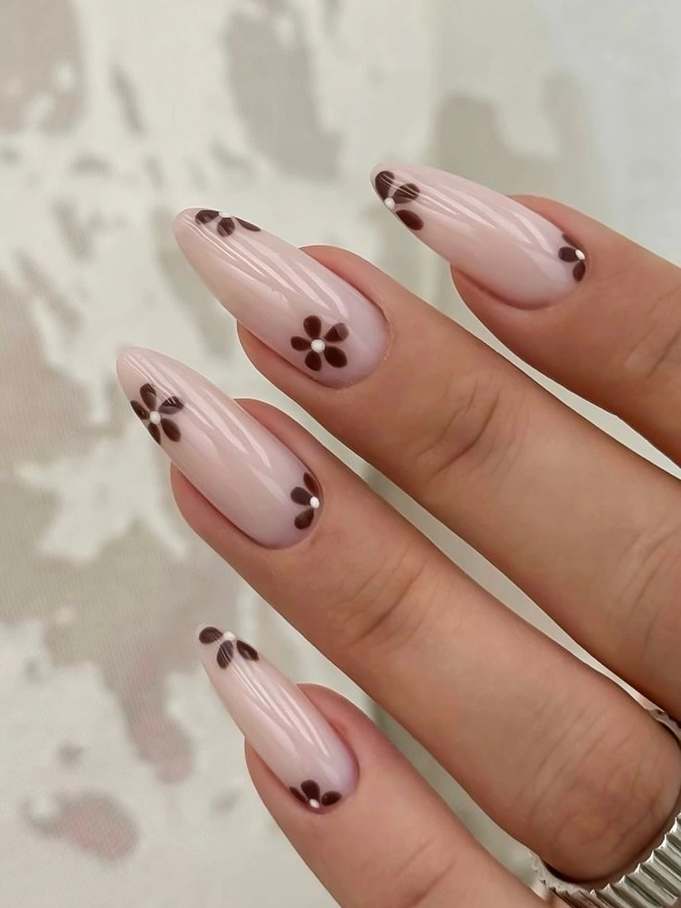 Glossy blush almond nails with simple brown daisy accents