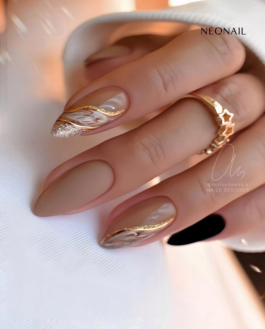 Beige almond nails with gold waves and black accent