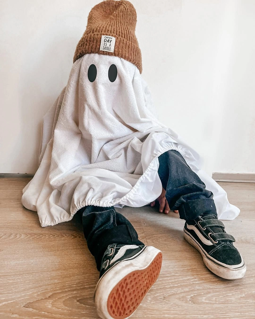 Child sheet ghost costume with brown beanie, jeans, and sneakers