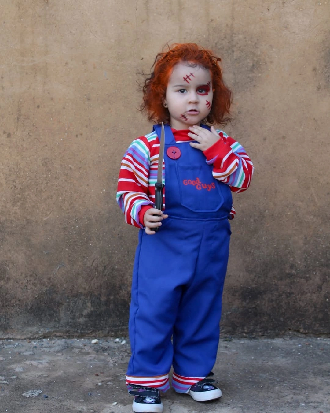 Chucky toddler costume with orange hair, striped shirt, blue overalls, and toy knife