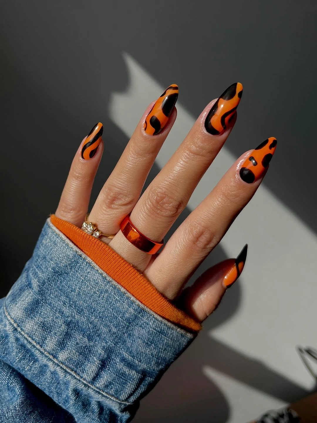 Orange and black curved flame accents on nude almond nails