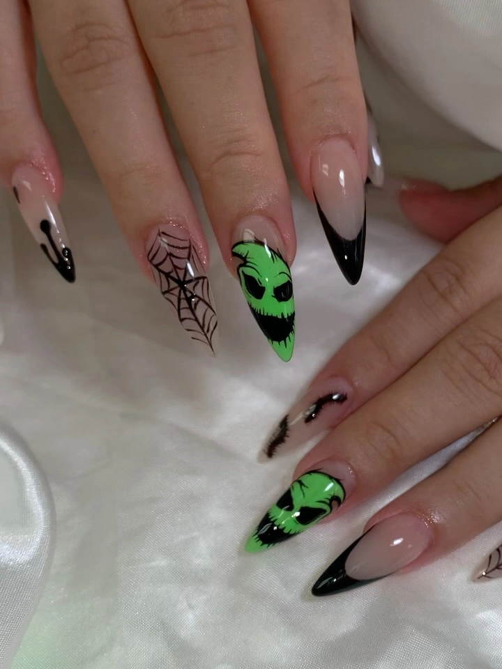 Nude almond nails with black tips, webs, and neon green faces