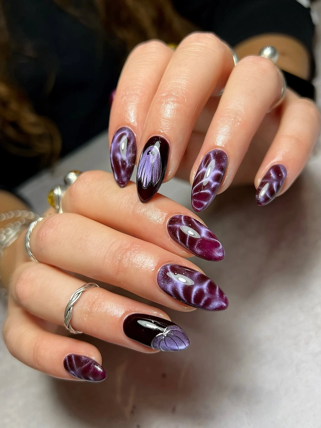 Plum almond nails with reflective wavy bands and butterfly detail