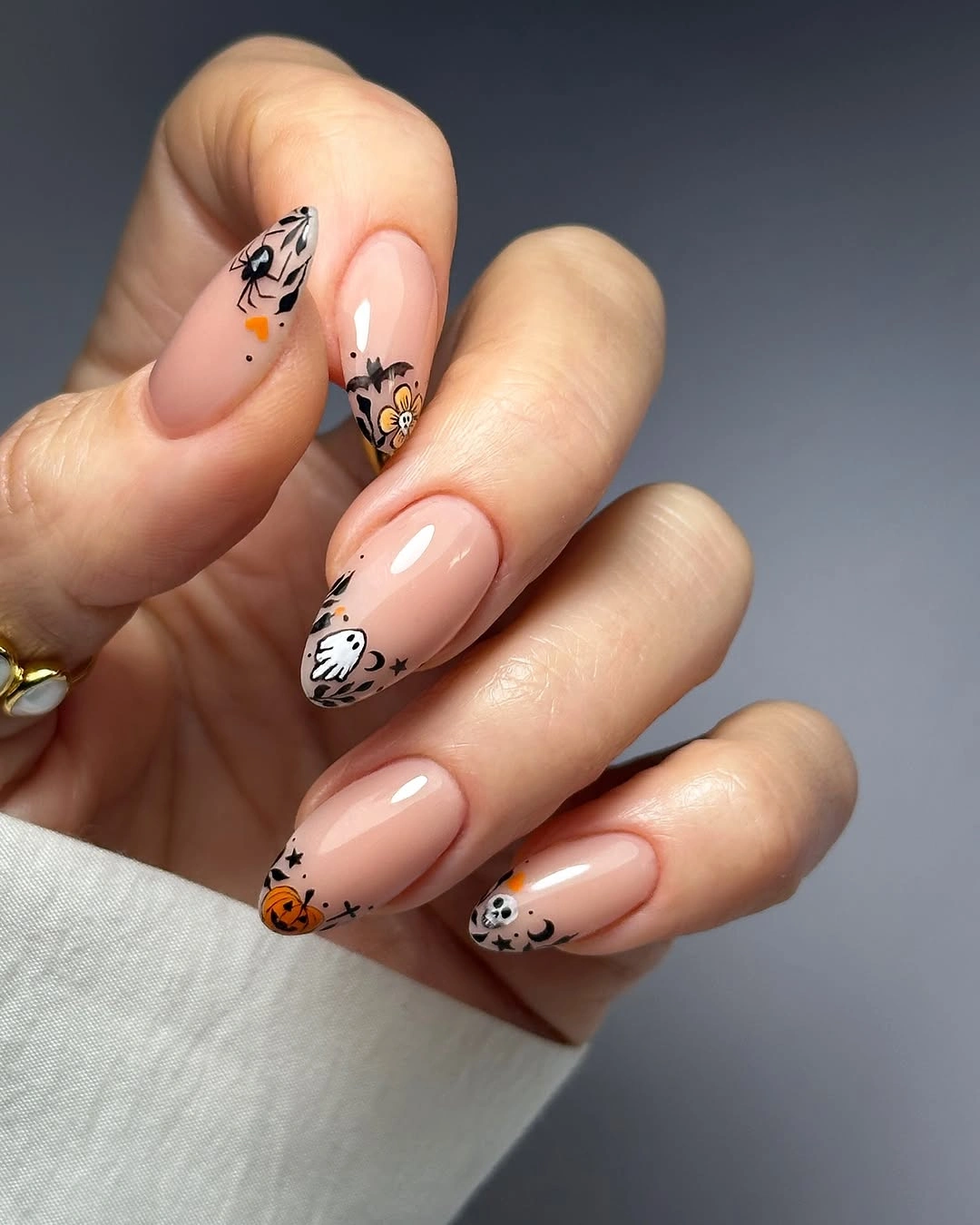 Nude almond nails with tiny spooky faces and pumpkin accents