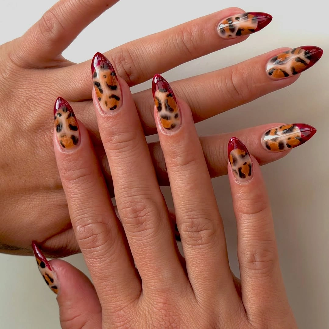 long nude pointed nails with red orange animal-print-like patches and dark outlines