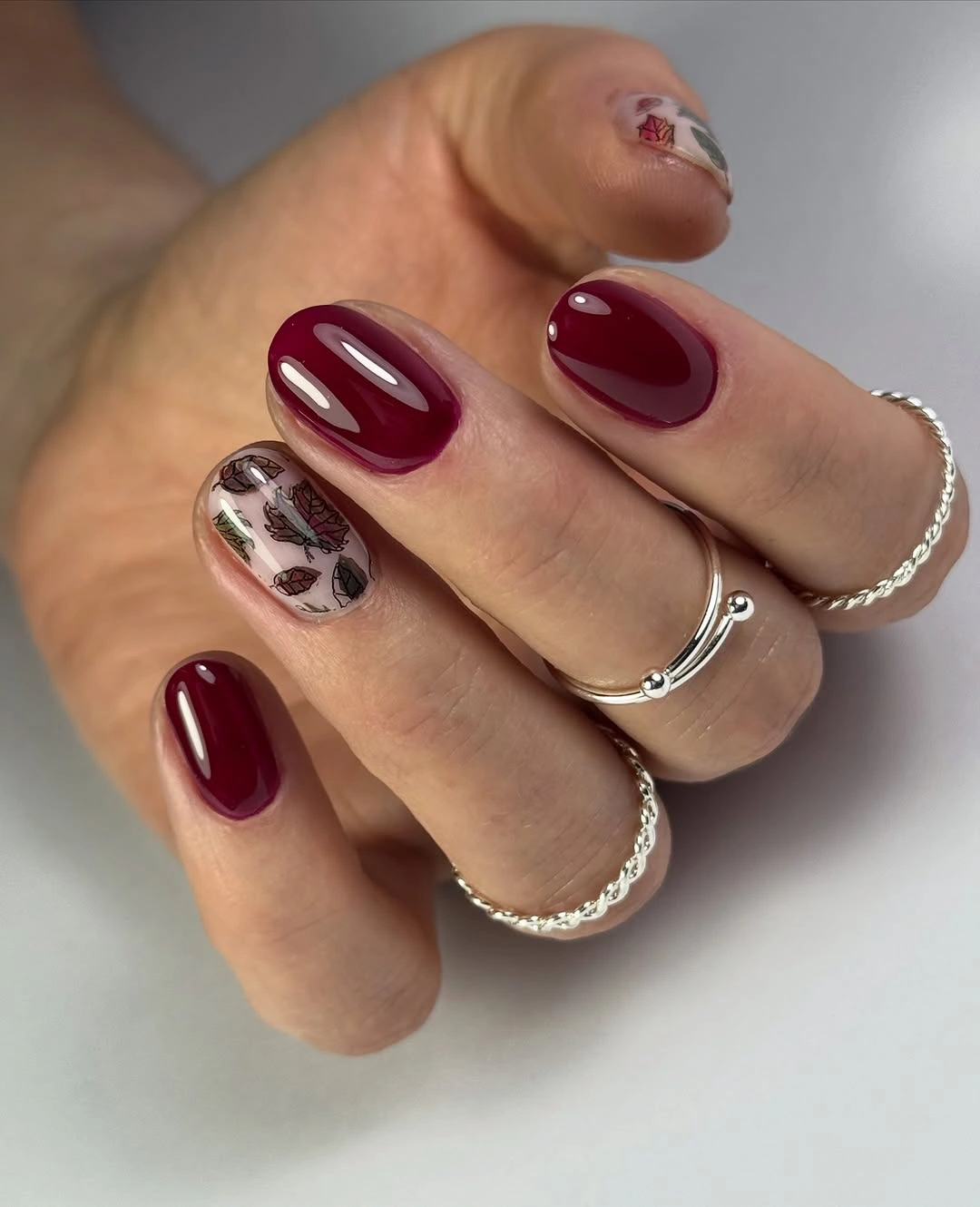 short glossy burgundy nails with one pale irregular spotted accent nail
