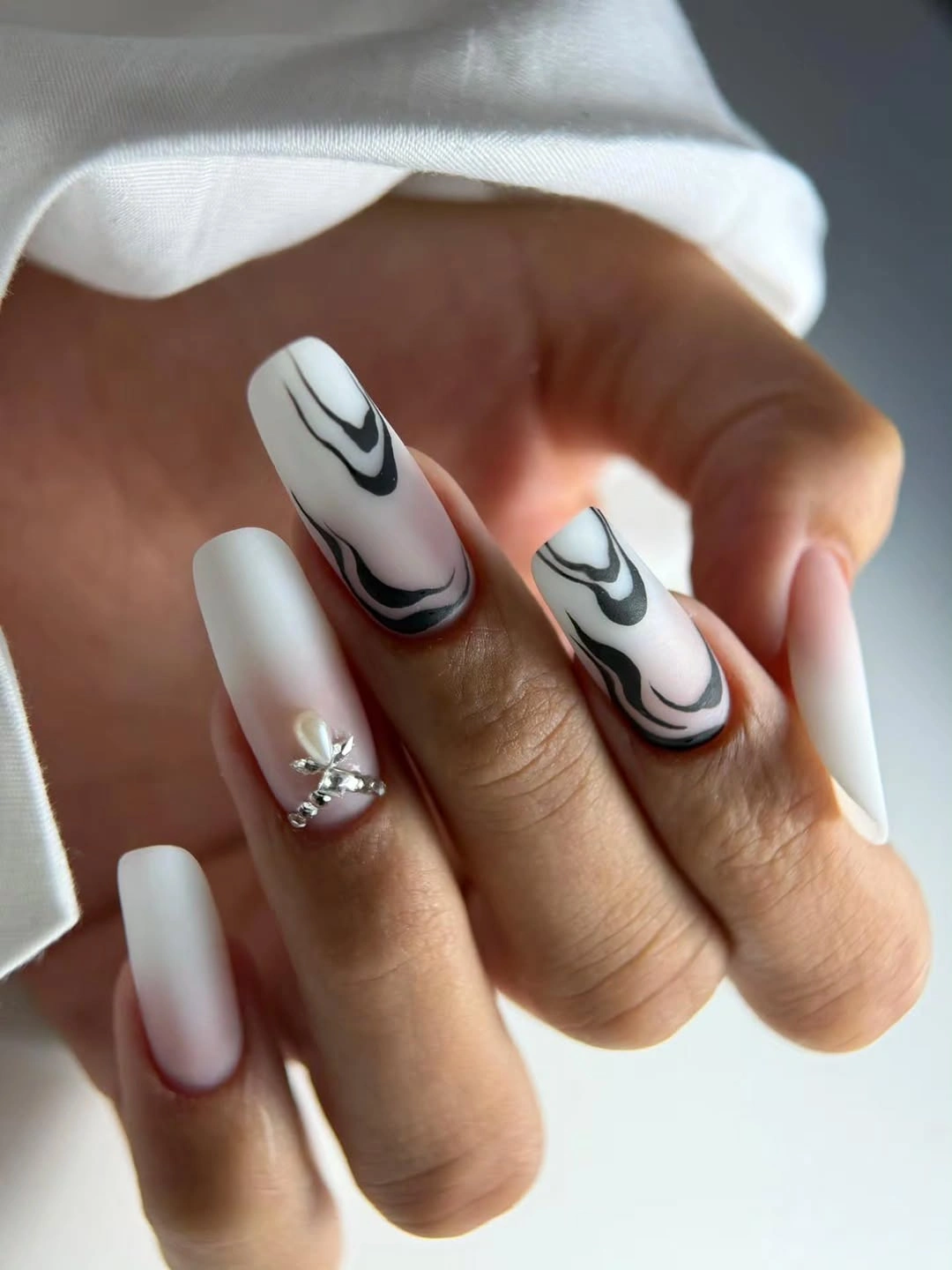 long matte white square nails with black abstract swirls and small reflective accent
