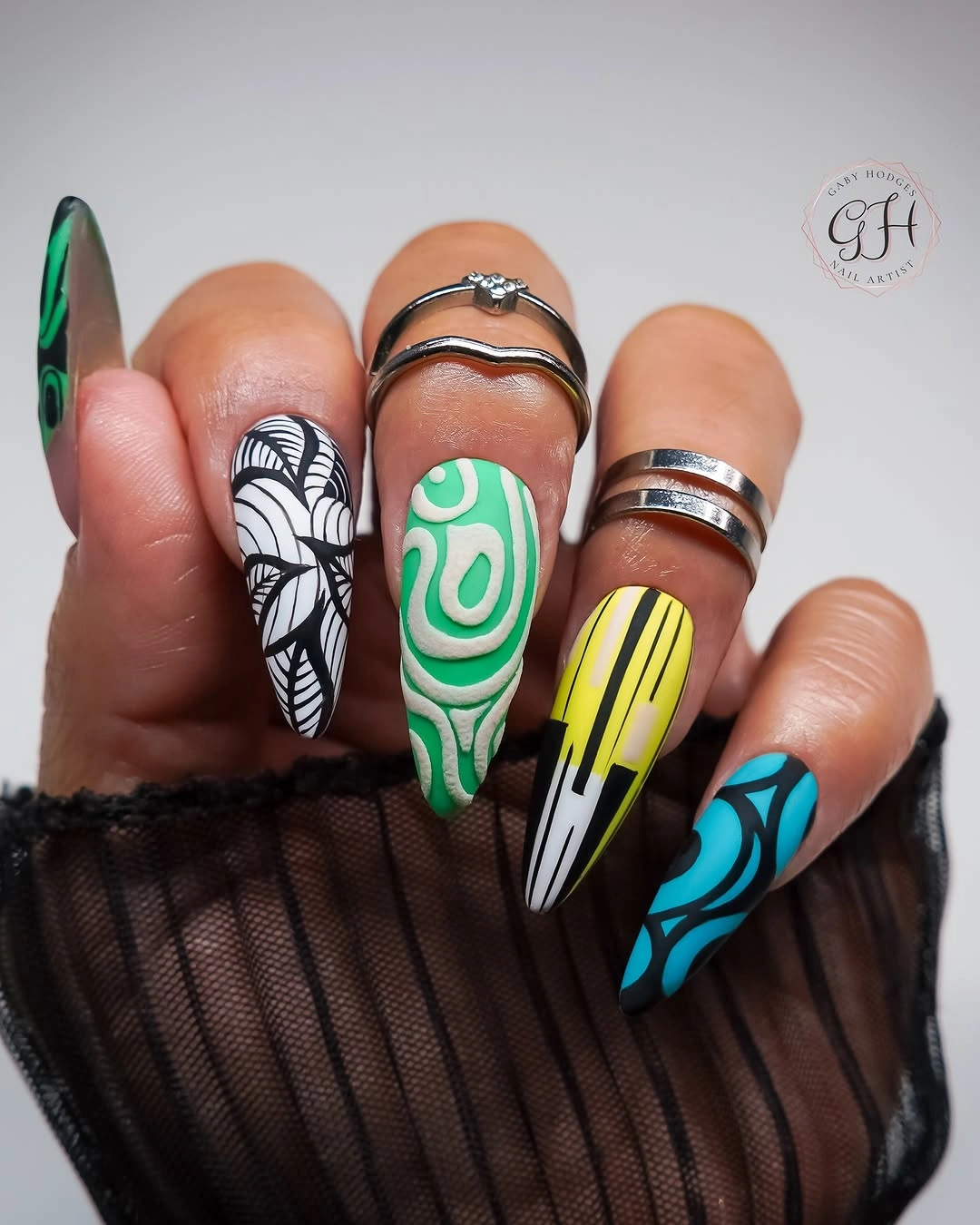 very long pointed nails with green swirls stripes yellow lines and teal graphic patterns