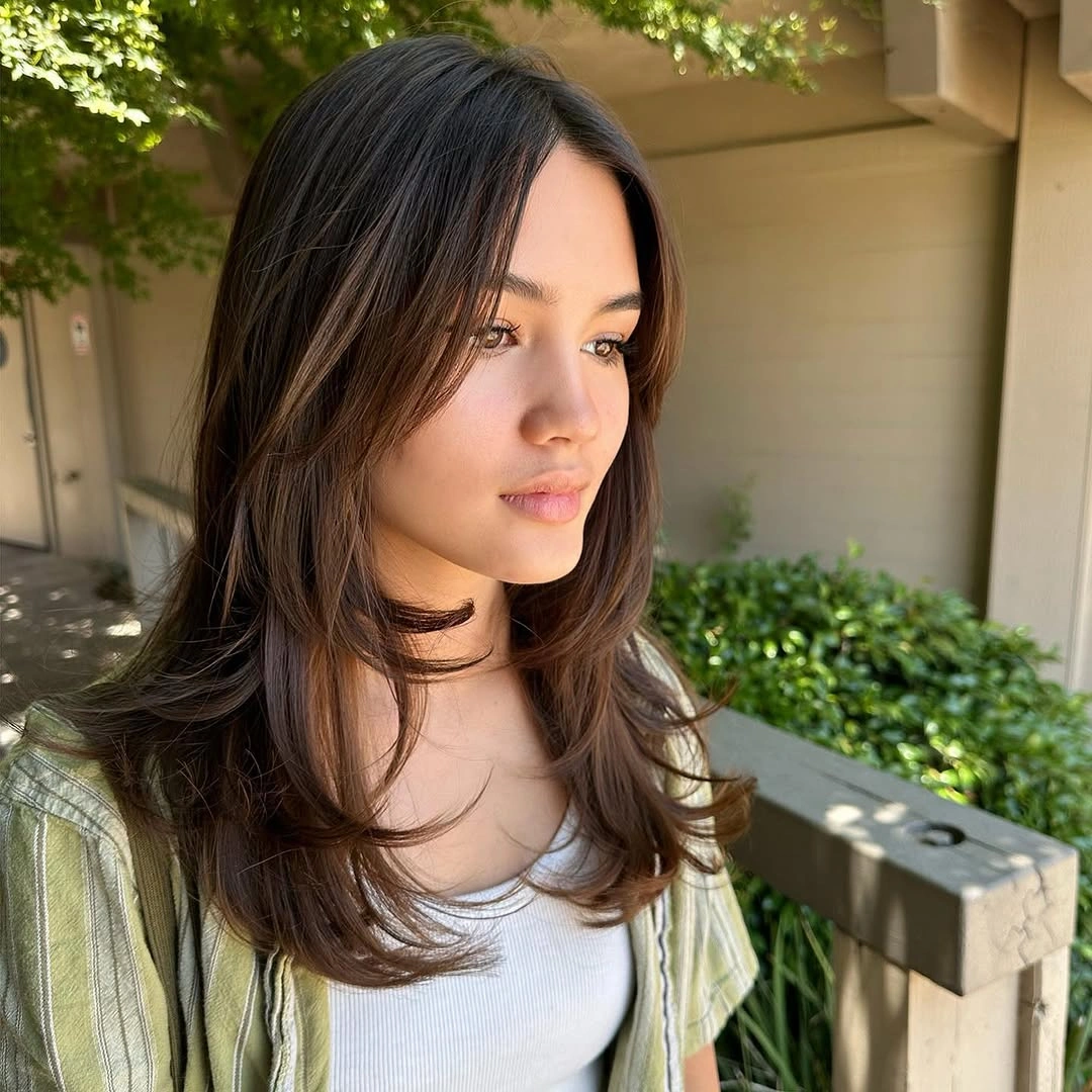 Medium dark center-parted hair with relaxed bends and soft layered ends