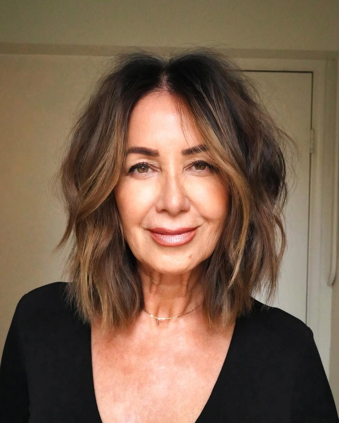 Medium dark hair with a center part, loose waves, and warm face framing