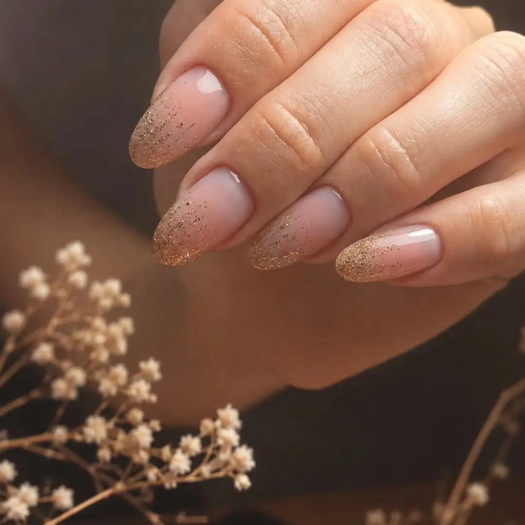 Sheer nude almond nails with warm champagne sparkle-like gradient toward the tips