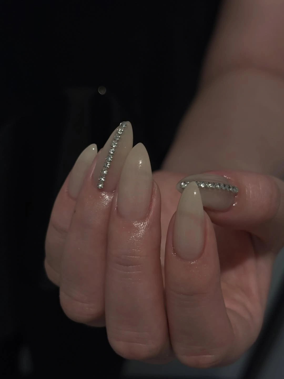 Long nude almond nails with clear-looking tips and small silver-toned accents