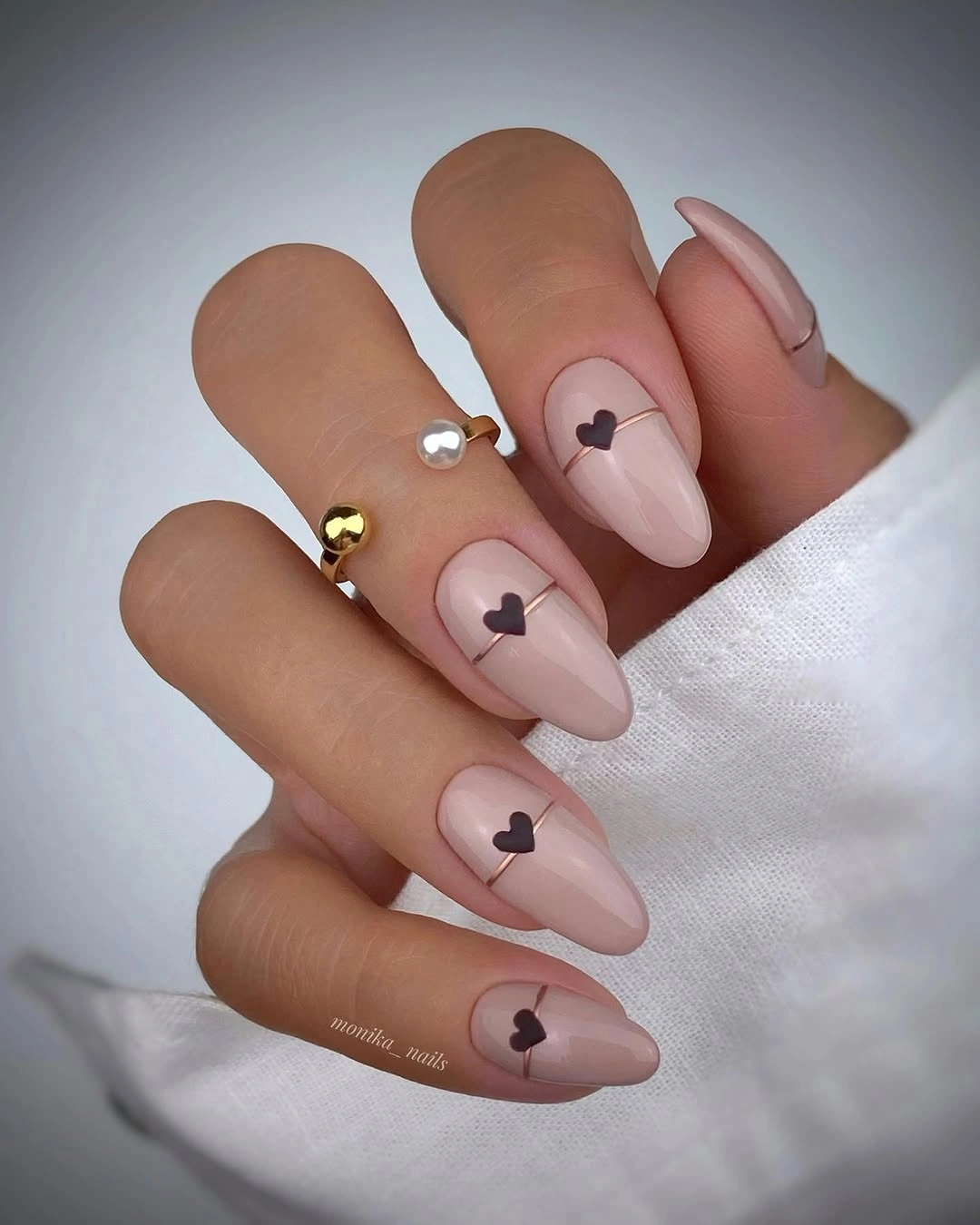 Warm nude almond nails with small dark heart-like marks and tiny gold-toned accents