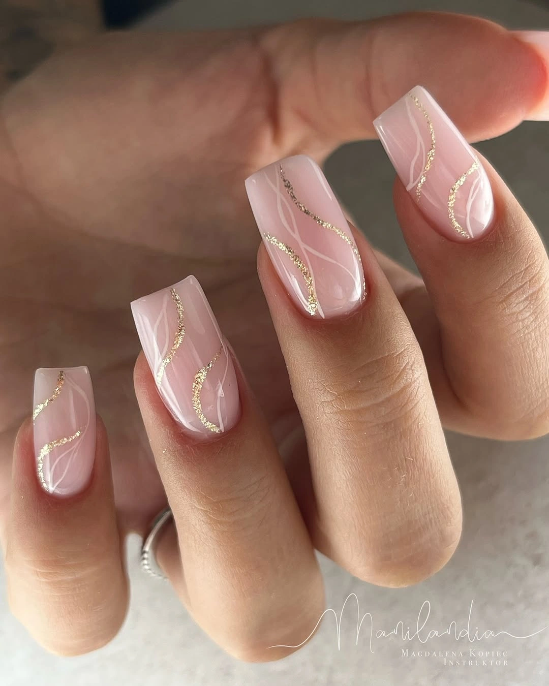 Pale pink square nails with thin white curves and slim gold-toned line details