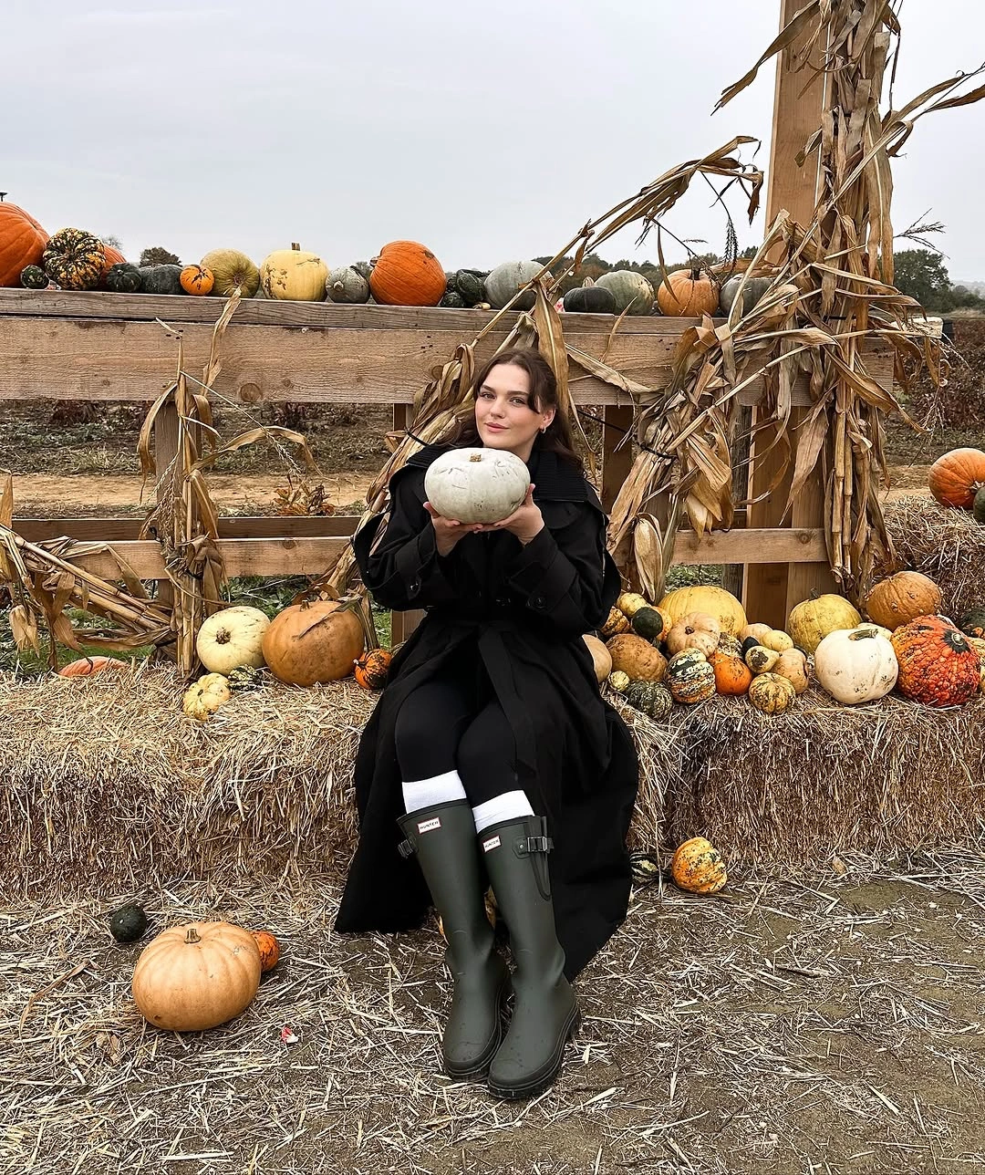 Black long coat with black boots holding a white pumpkin
