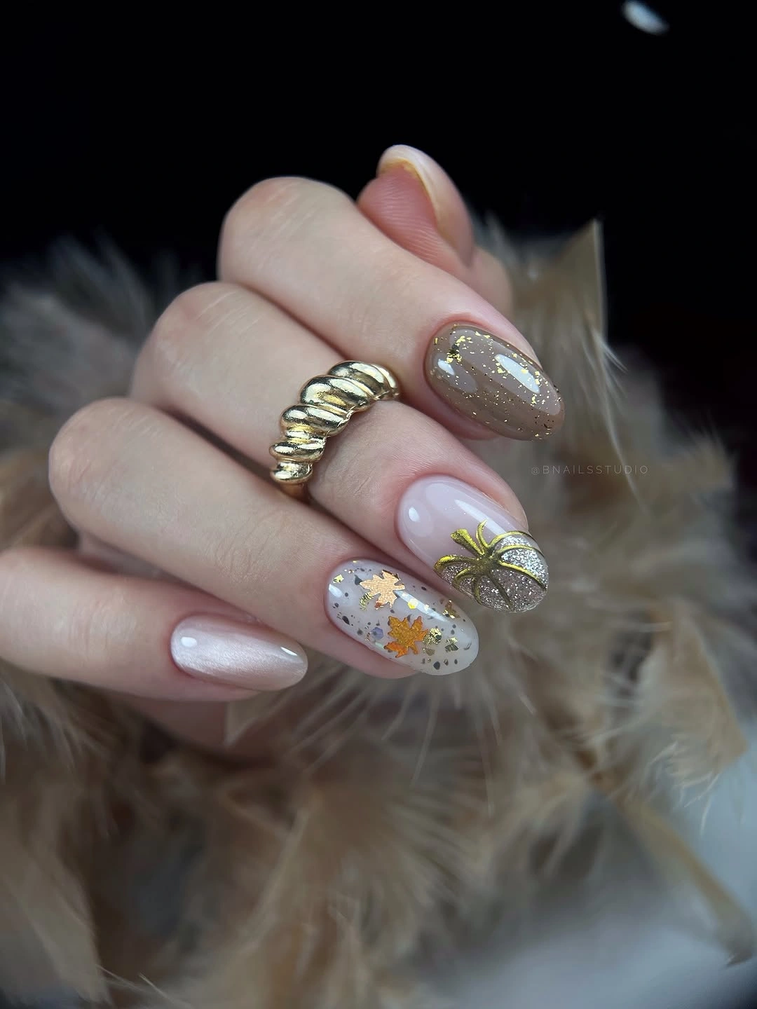Pale neutral almond nails with muted green and gold botanical accents