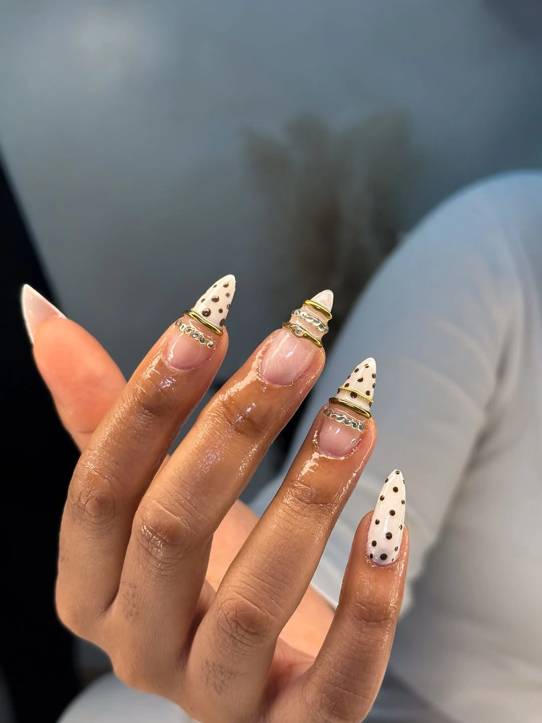 long nude almond nails with cream black dotted tips and one small gold-toned accent