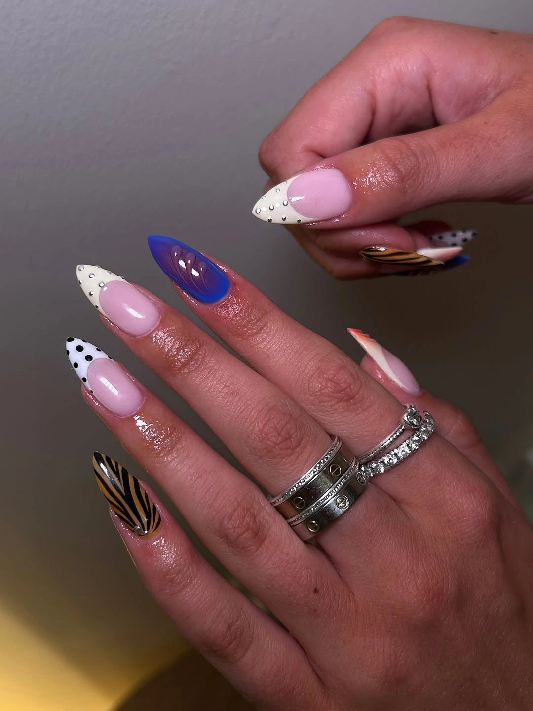 long pink nails with varied dotted tips blue accent black stripes and small gold detail