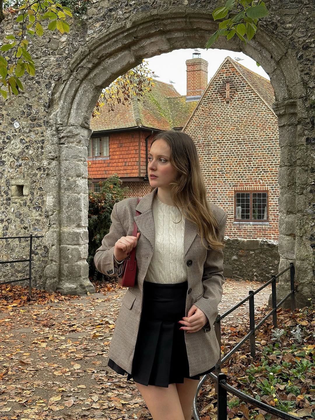 Gray blazer with cream sweater black pleated skirt and red bag