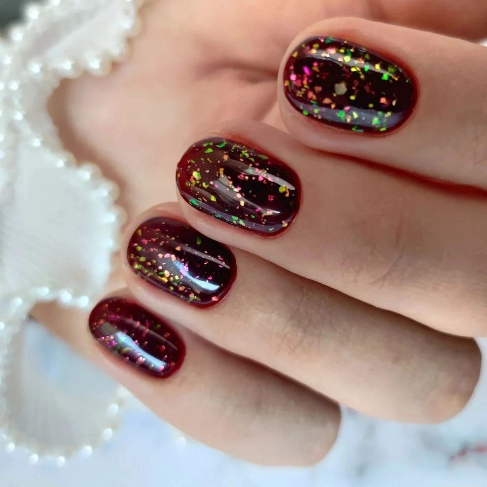 Short burgundy rounded nails with multicolor reflective flakes
