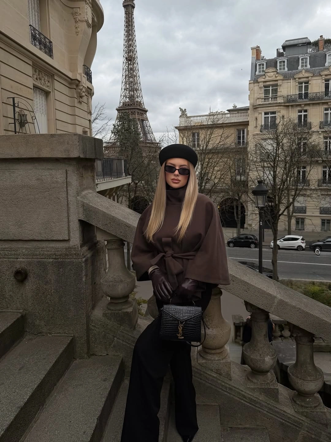 Brown belted cape-like top with wide black trousers and black accessories