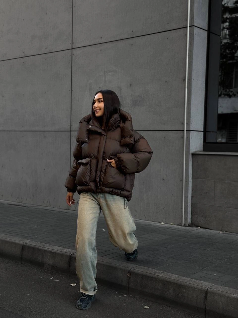 Brown puffer-style jacket with loose faded jeans and dark shoes