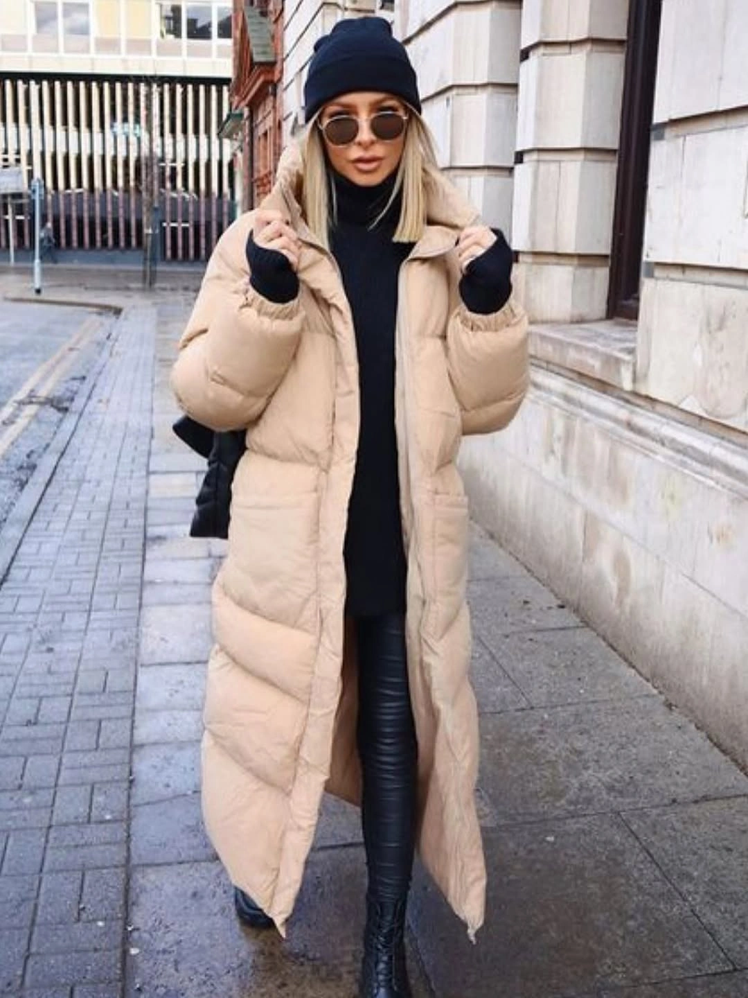 Long beige puffer-style coat over black top and shiny trousers