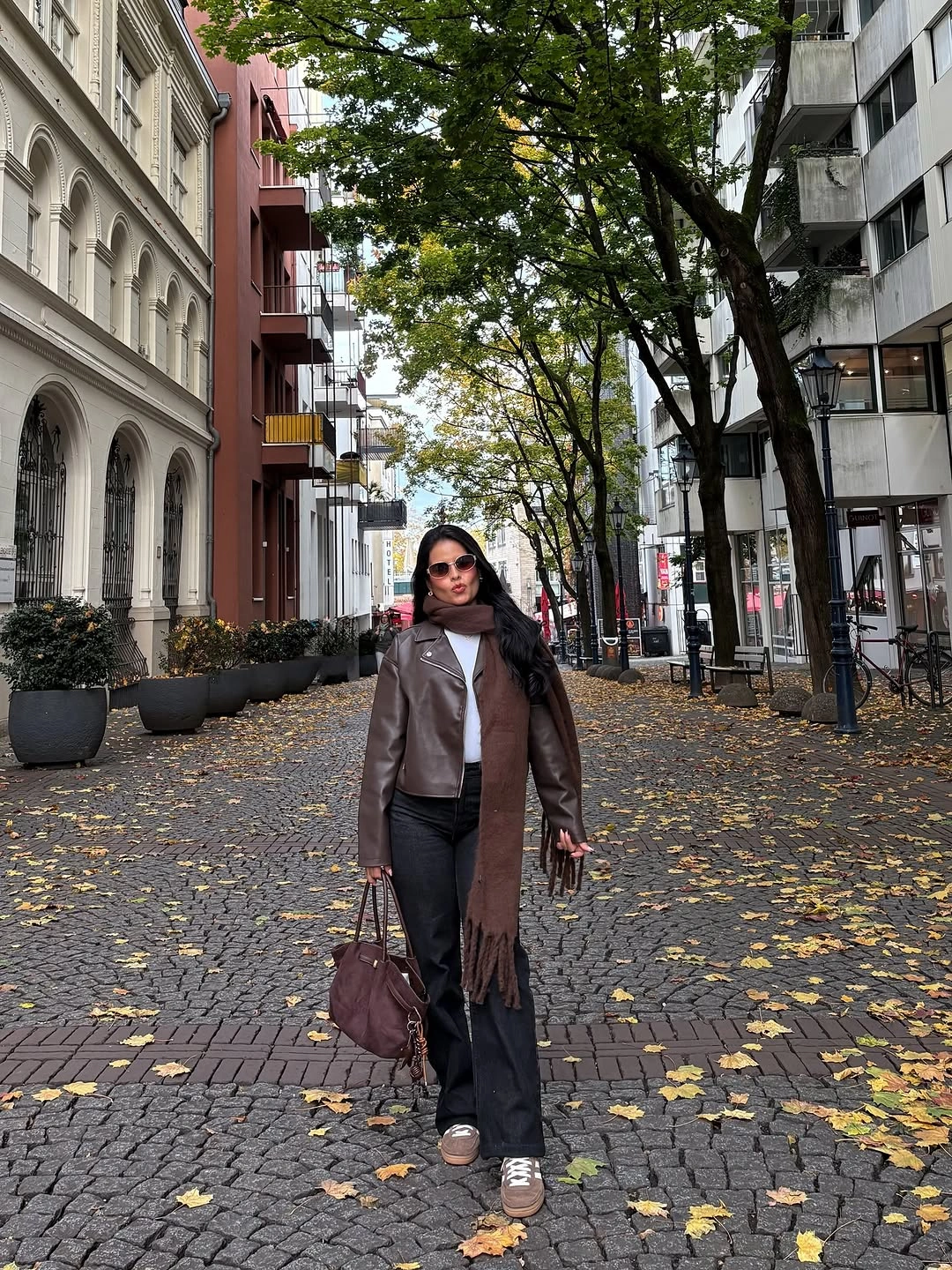 Brown leather-look jacket, long scarf, dark jeans, white top, and handbag