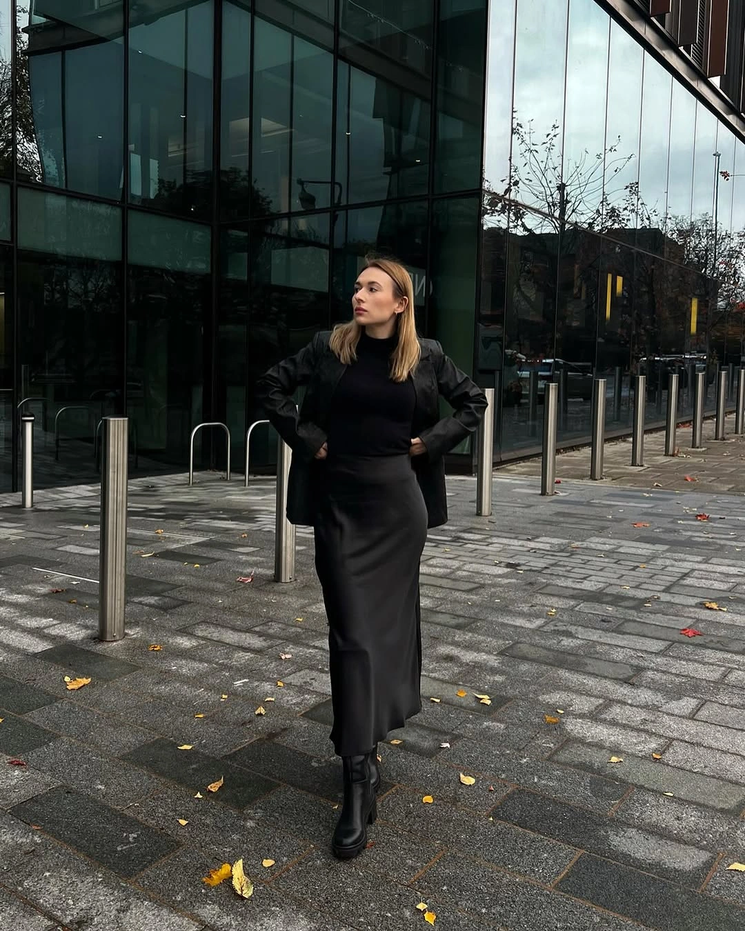 Black fitted top, jacket, smooth midi skirt, and ankle boots