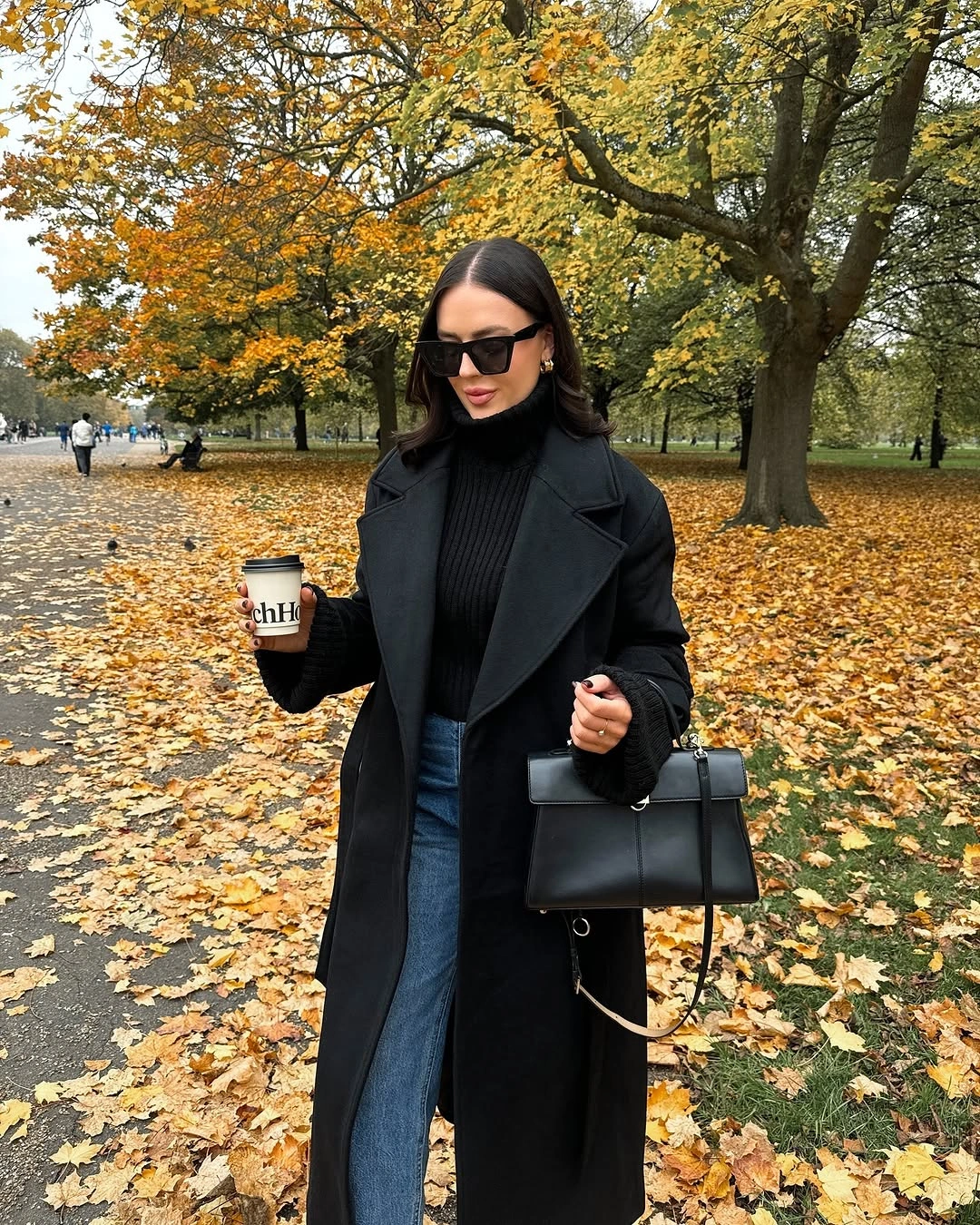 Long black coat, black high-neck top, blue jeans, and structured handbag