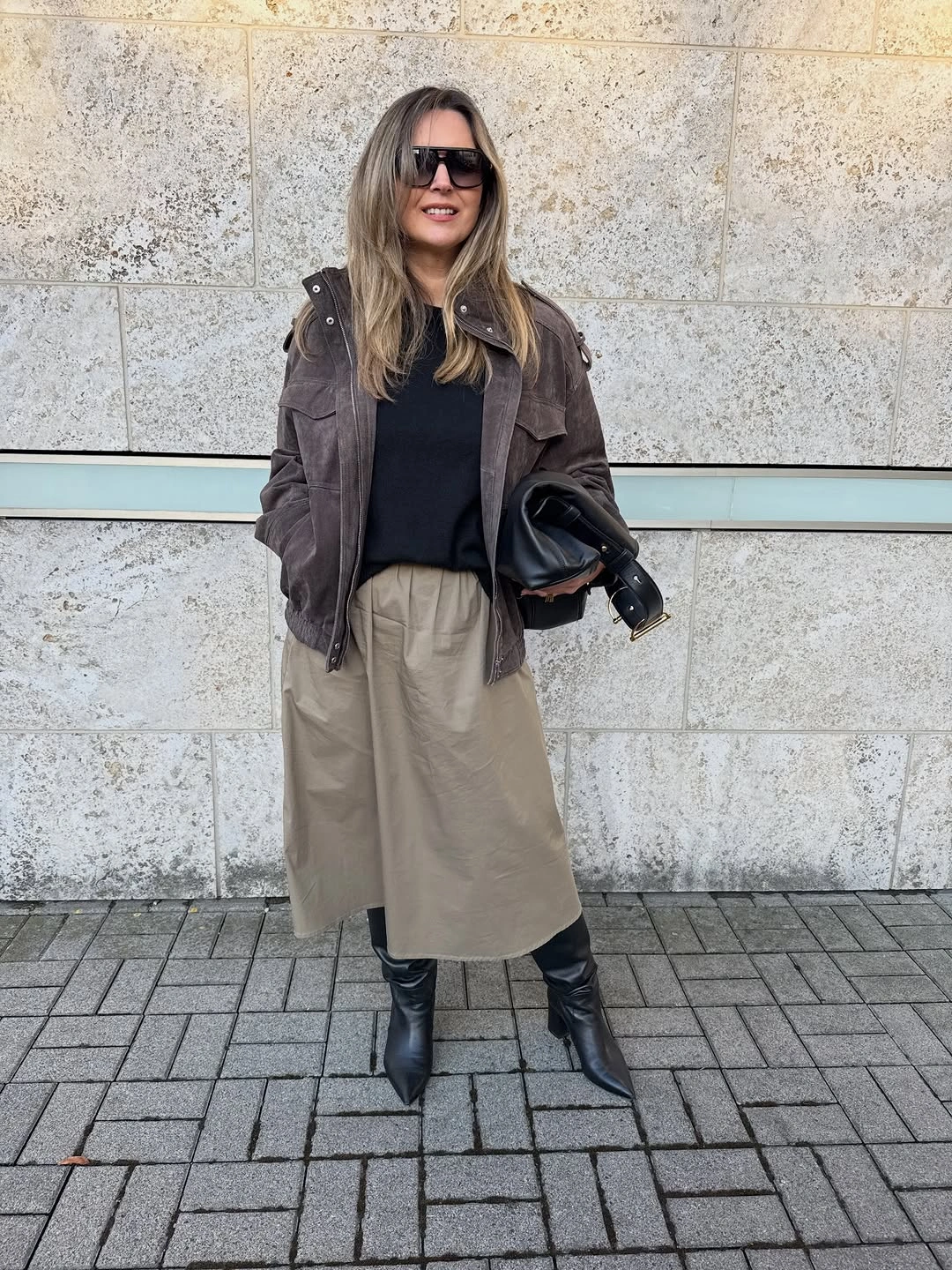 Gray-brown jacket, beige midi skirt, black top, bag, and tall boots