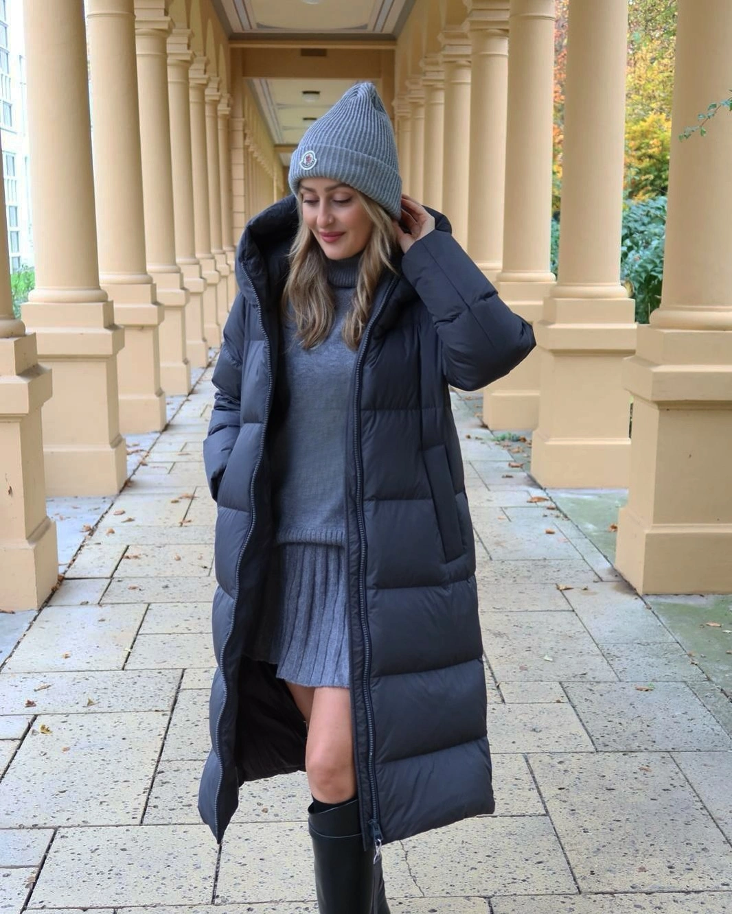 Navy puffer-style coat over blue pleated skirt and black boots