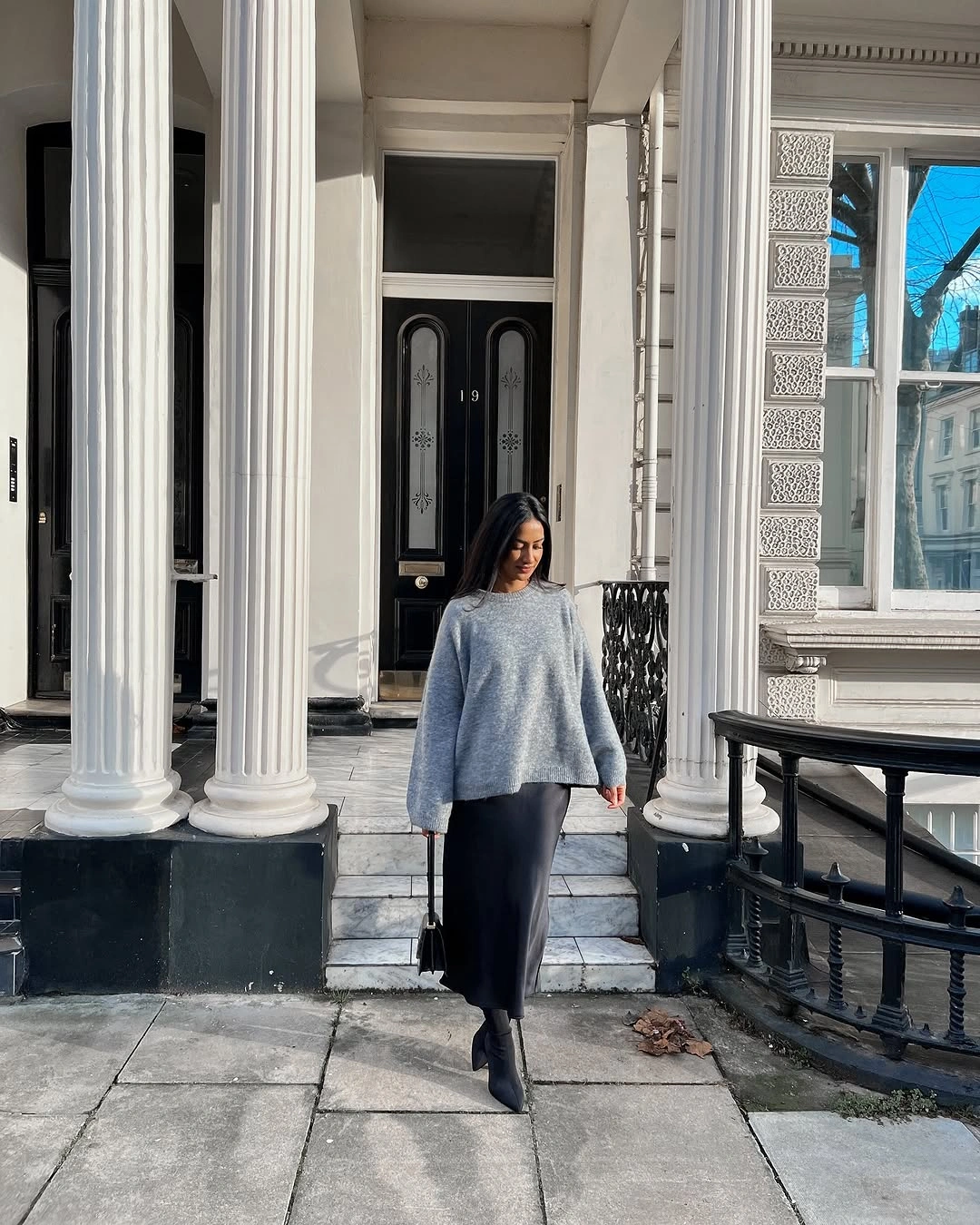 Gray sweater with lustrous black midi skirt, boots, and handbag