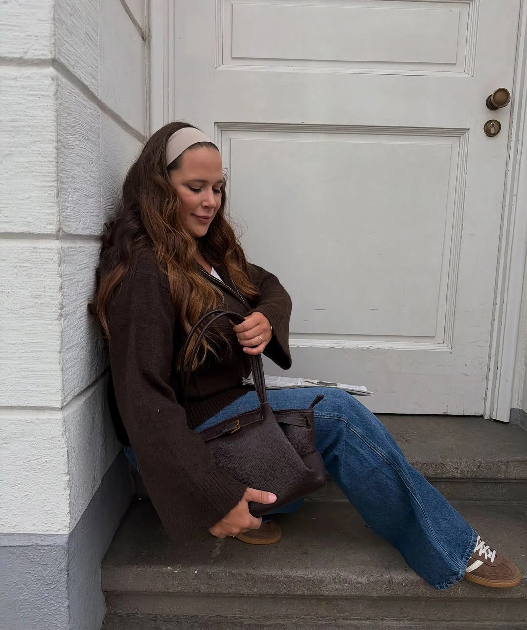 Dark brown oversized top, blue jeans, large tote, sneakers, and headband