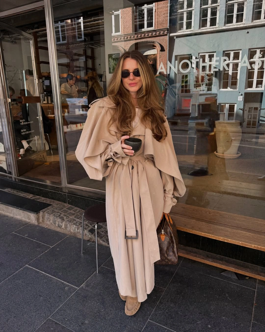 Long beige belted coat with cape-like overlay, brown tote, and tan footwear