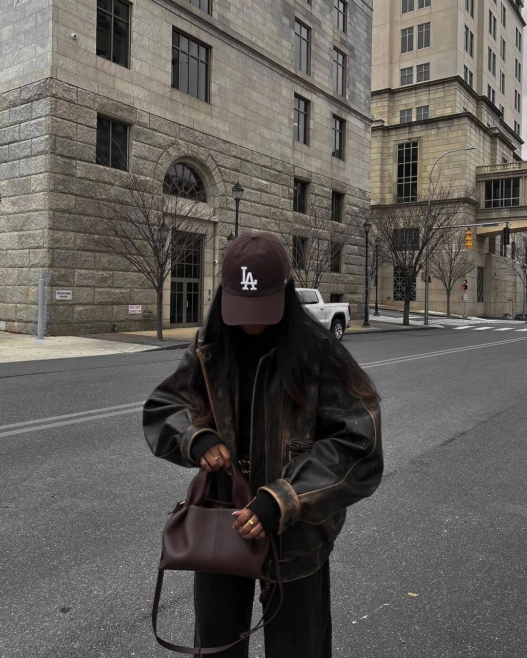 Dark brown leather-look bomber, black lower half, brown cap, and handbag