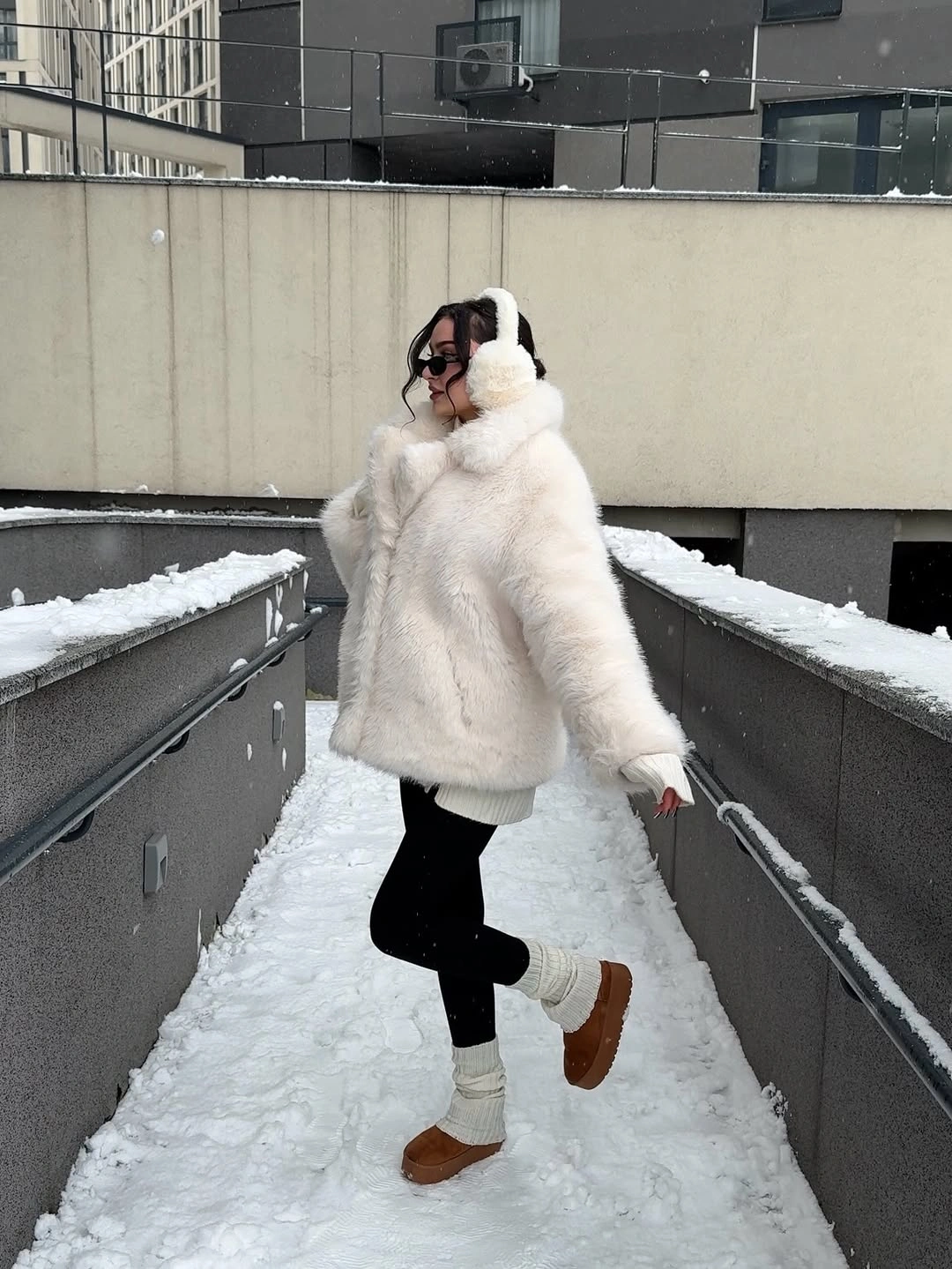 Ivory fluffy jacket, pale headwear, black leggings, white ribbed socks, and brown rounded boots.