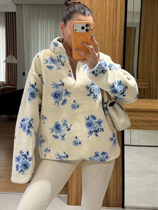 Cream zip-neck pullover with blue motifs, fitted cream trousers, and a small cream shoulder bag.