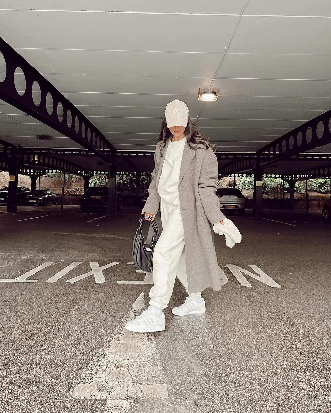 White hoodie and joggers under long grey coat with white sneakers and black handbag.