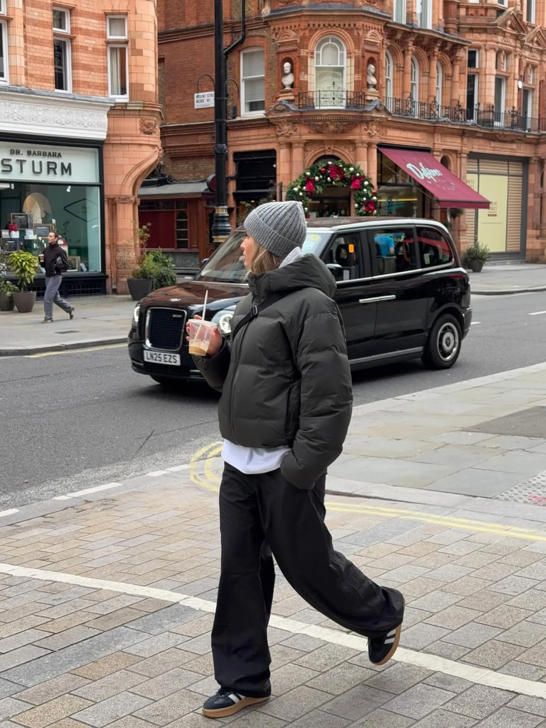 Short black puffer, gray beanie, white hem, loose black trousers, and black sneakers.