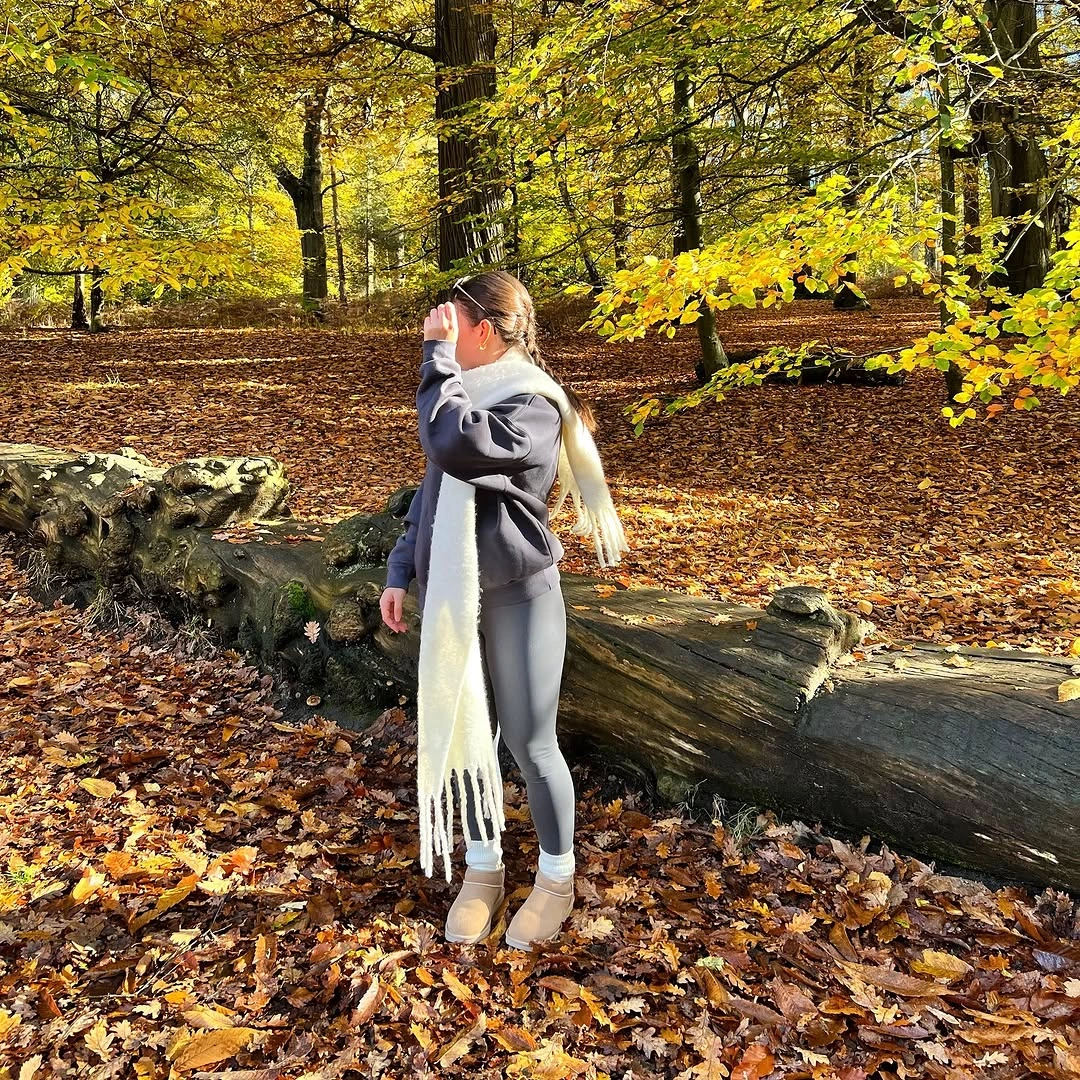 Long gray-taupe outer layer, cream fringed scarf, slim gray pants, and beige ankle boots.